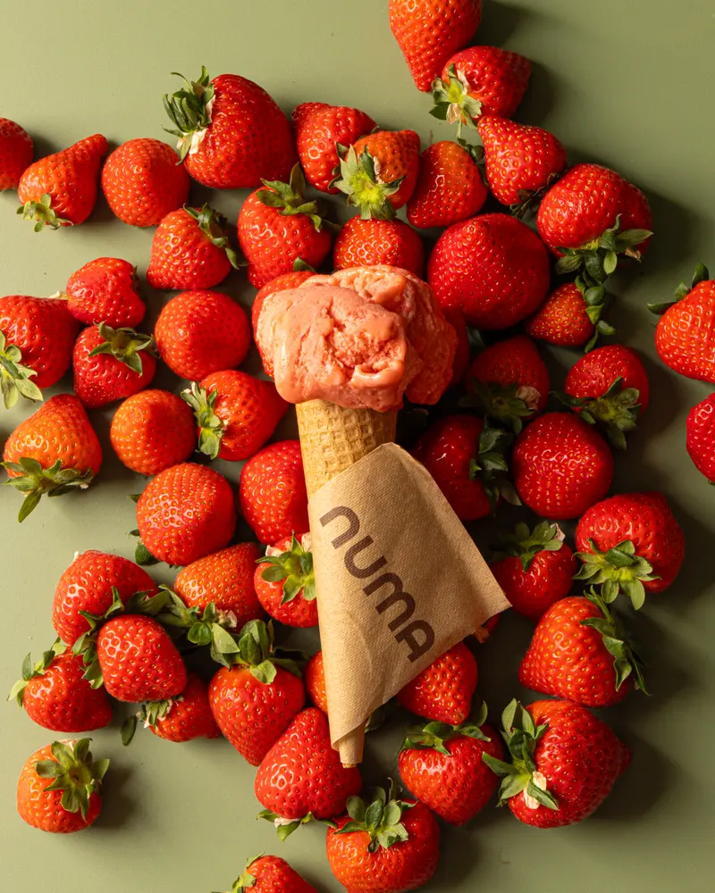 Cono di gelato alla fragola Numa avvolto nel tovagliolino, tra fragole fresche